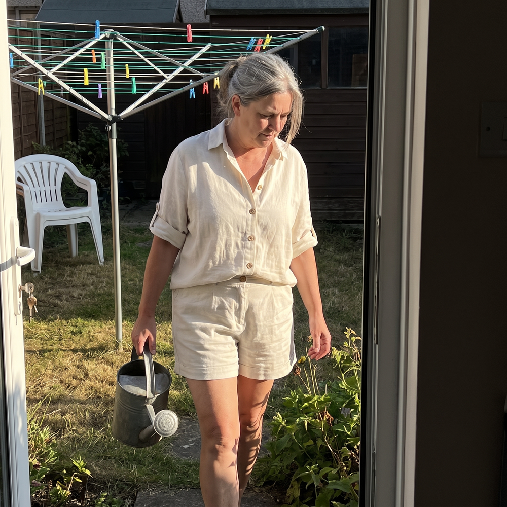 Customer wearing the Melda cream linen shirt and shorts set watering the garden